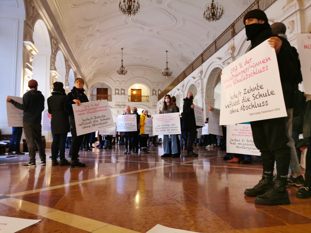 Fachkräfte stehen mit Schildern im Rathaus und demonstrieren.